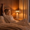 Lampe Oréa en travertin et verre transparent allumée sur une table de chevet, ambiance chambre chaleureuse